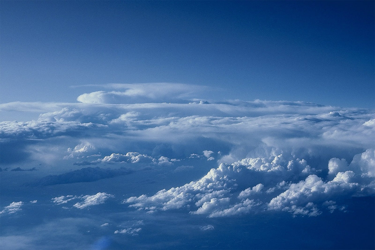 Layers of white clouds stretch across a blue aerial view through an aircraft window.