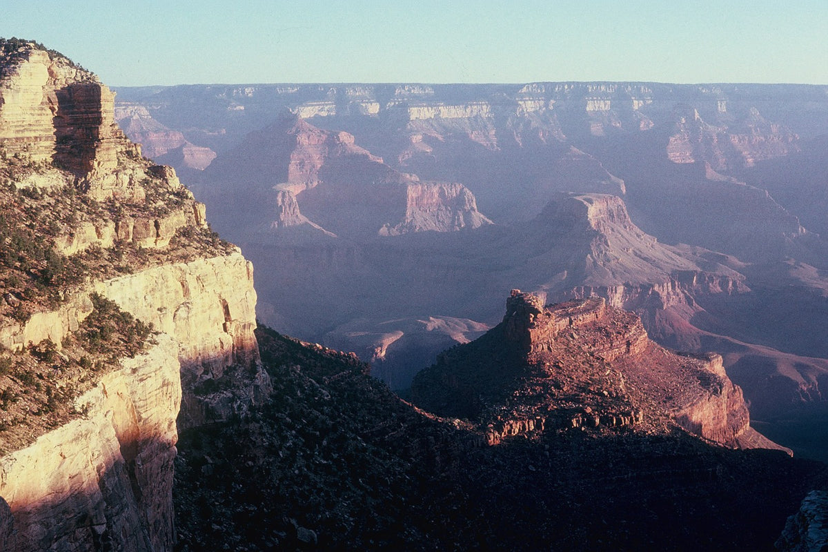 Evening light warms layered cliffs and deep shadowed ravines in the Grand Canyon.