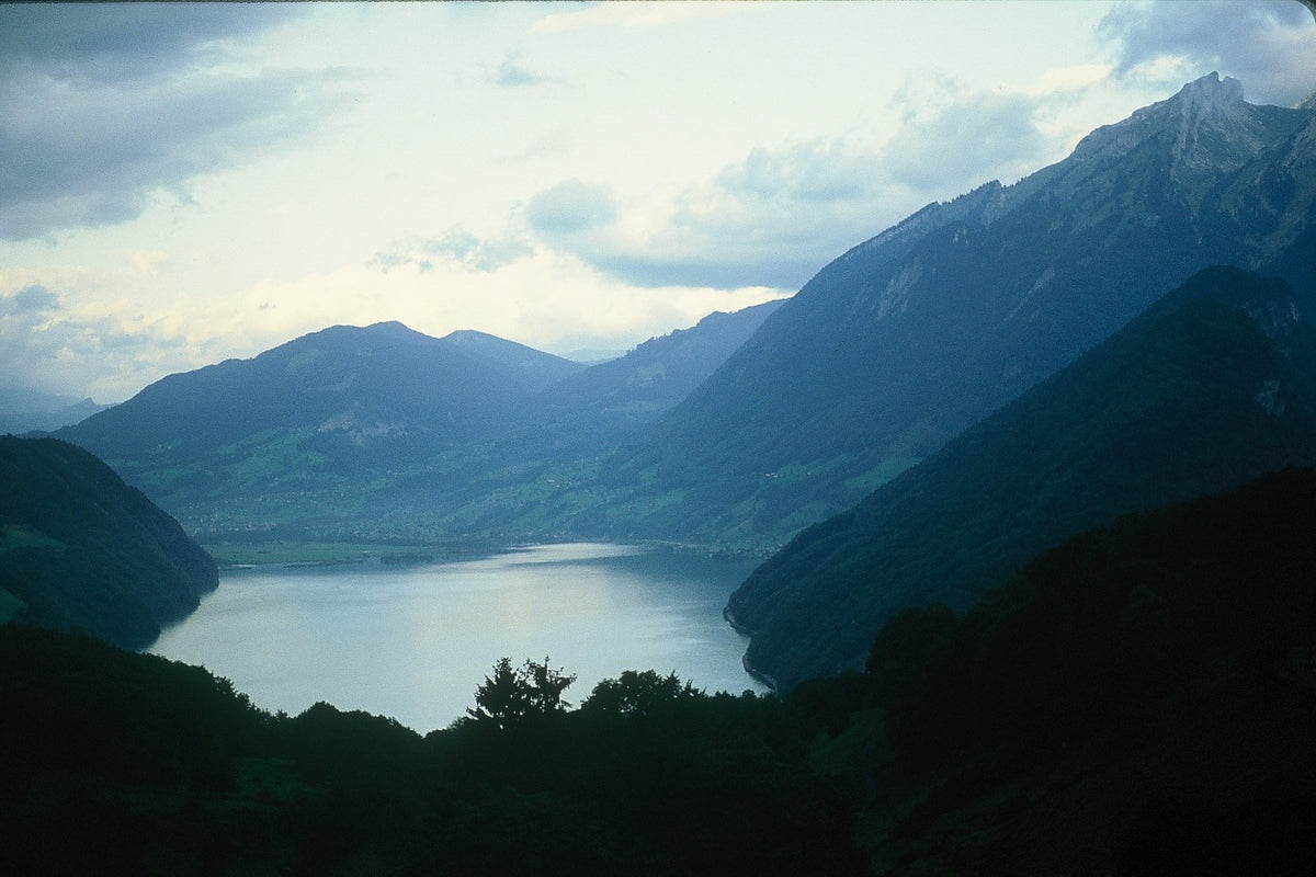 A pale blue Swiss lake lies between dark slopes beneath a softly clouded sky.