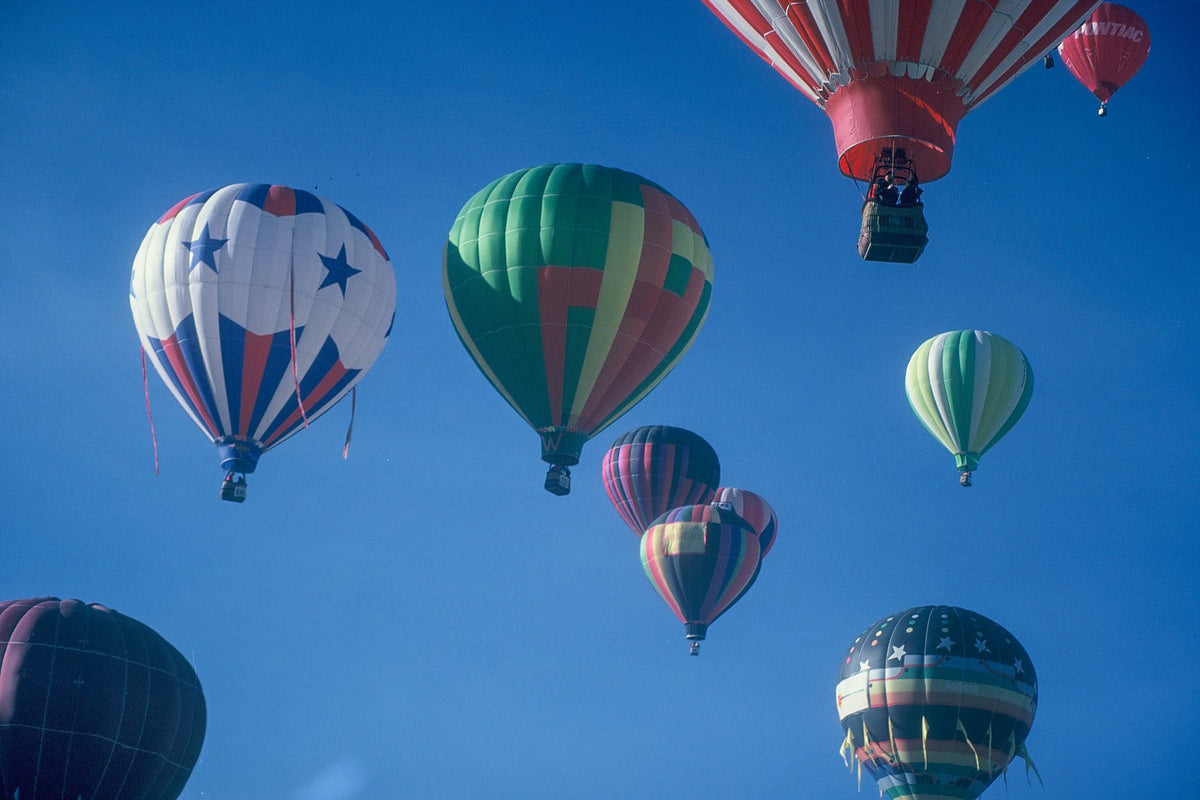 Brightly patterned hot air balloons rise against blue sky during a mass ascension in Albuquerque.