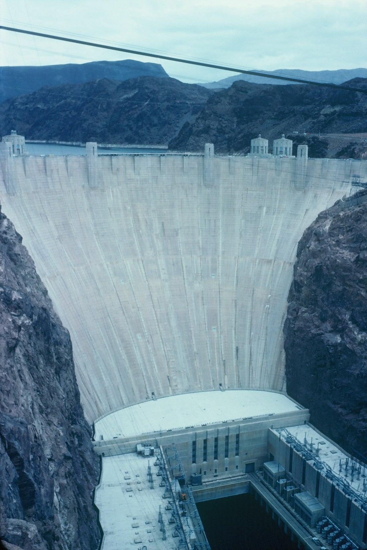 The curved concrete face of Hoover Dam spans a rocky canyon above the power station.