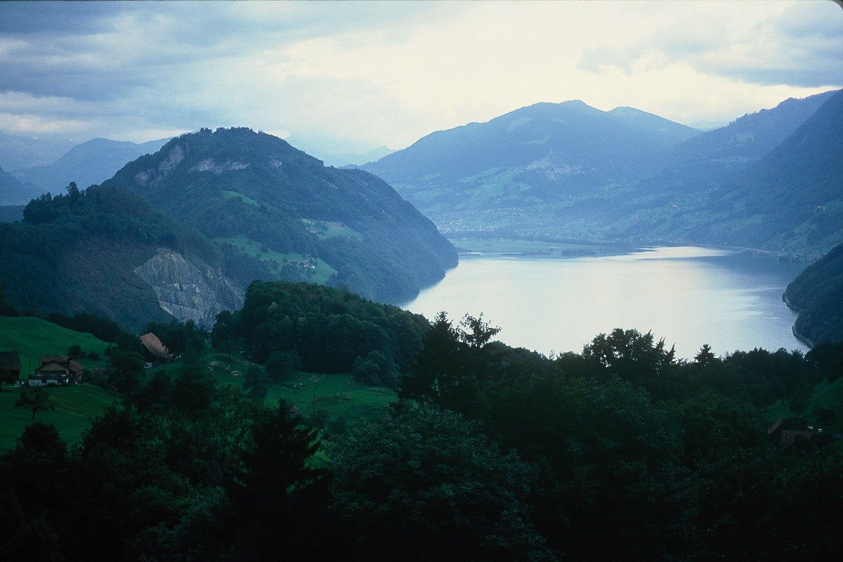A Swiss mountain lake curves through a valley below forested hills and layered distant ridges.
