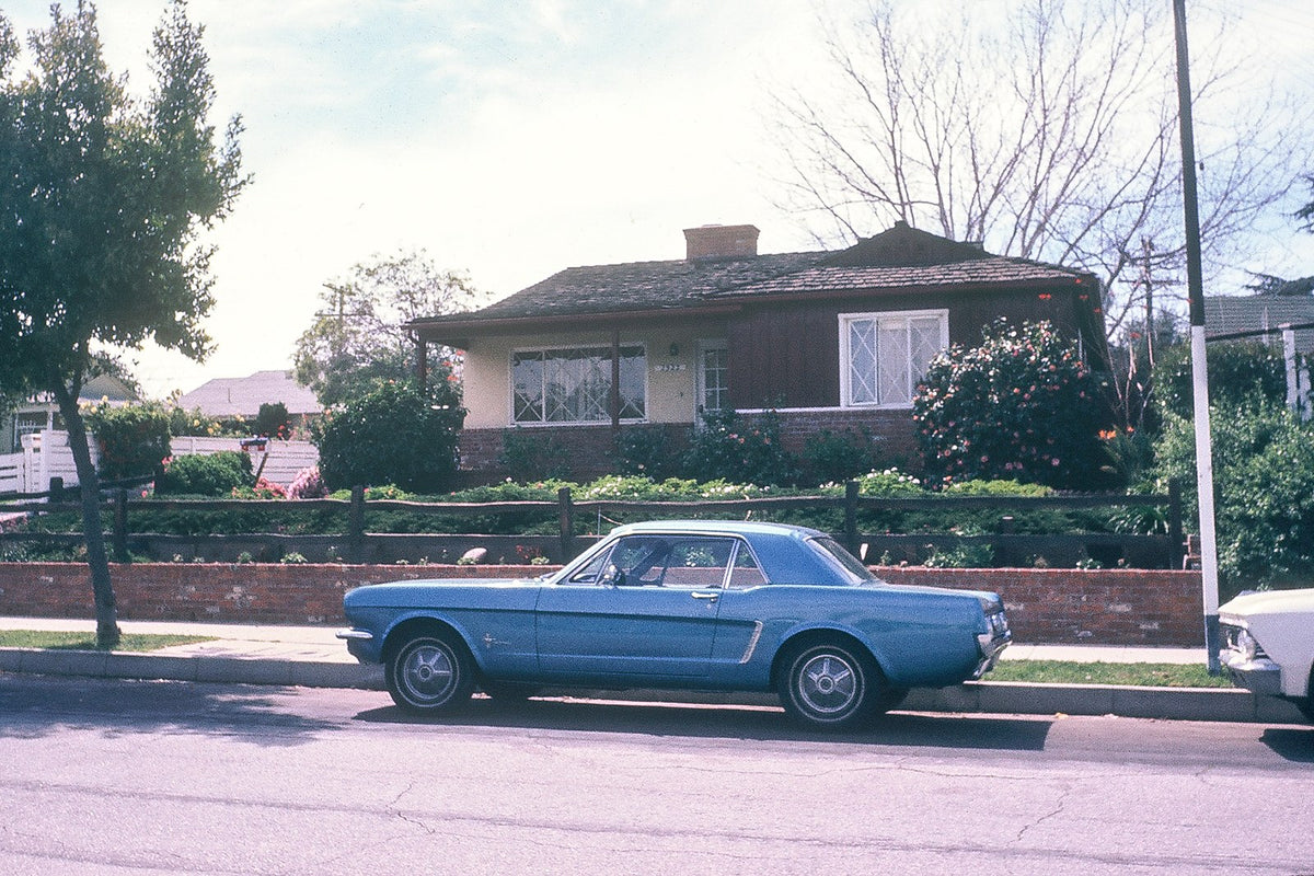 A blue 1965 Ford Mustang is parked along a residential street in front of a Santa Monica home.